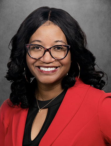 Photo of Tori Collier wearing a bright red blazer and black and amber glasses